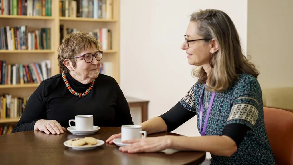 lady talking to a member of staff at Jewish Care over a cup off tea.