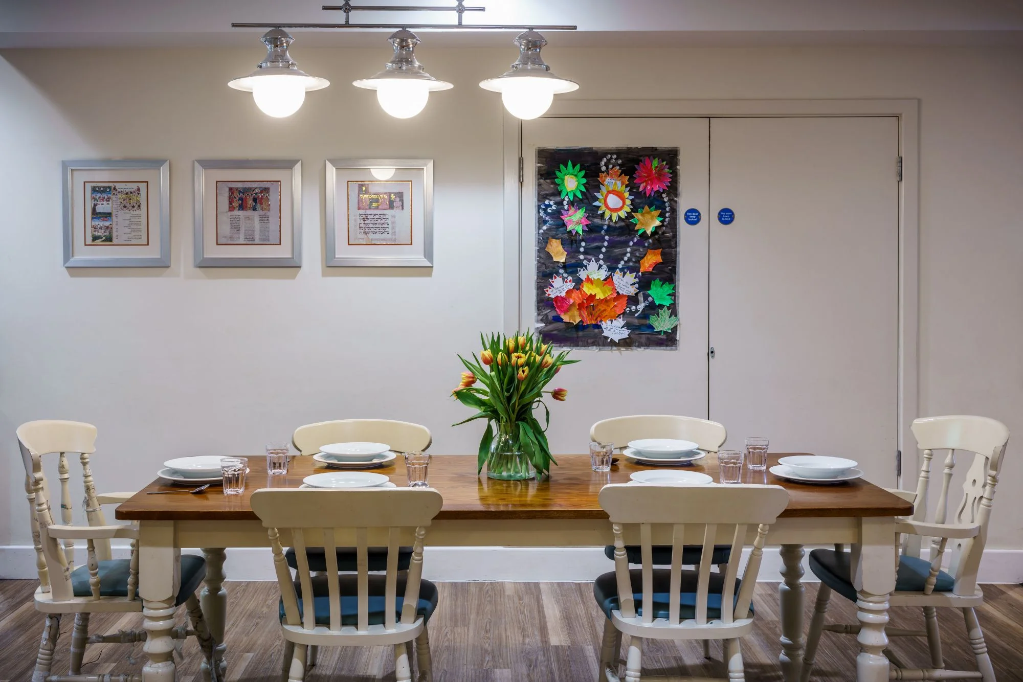 A large farmhouse-style table with flowers and pictures on the wall behind