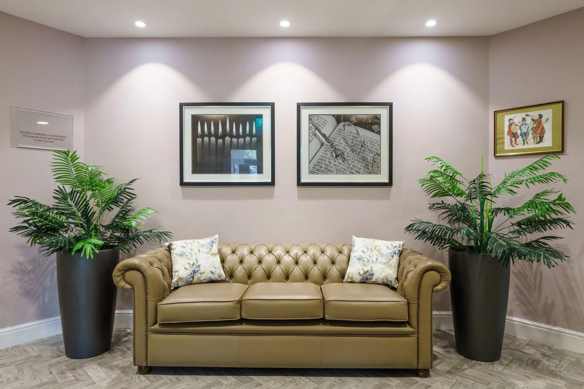 A brown chesterfield sofa surrounded by plants and pictures on the wall